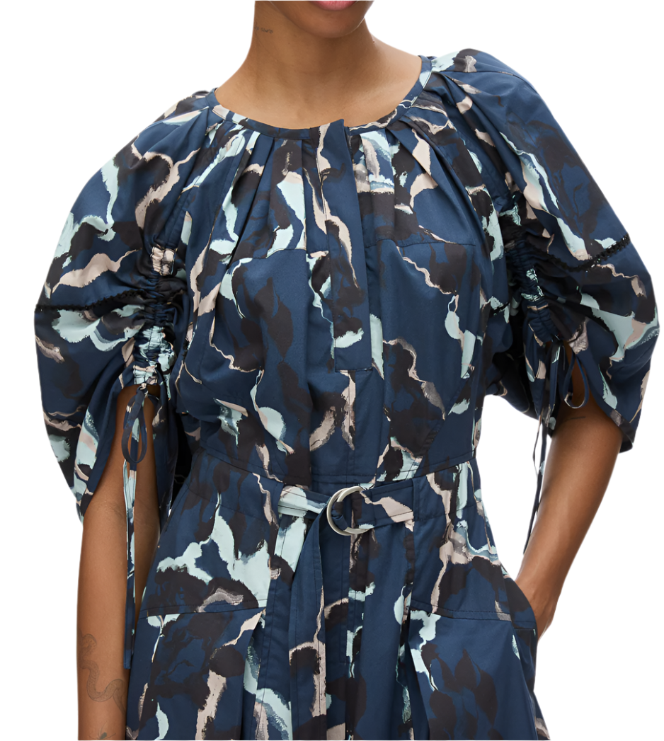 A person is wearing the 3.1 Phillip Lim Abstract Vines Belted Dress, which features a blue, black, and white pattern with abstract vines, puff sleeves, a cinched waist, and a tiered skirt.