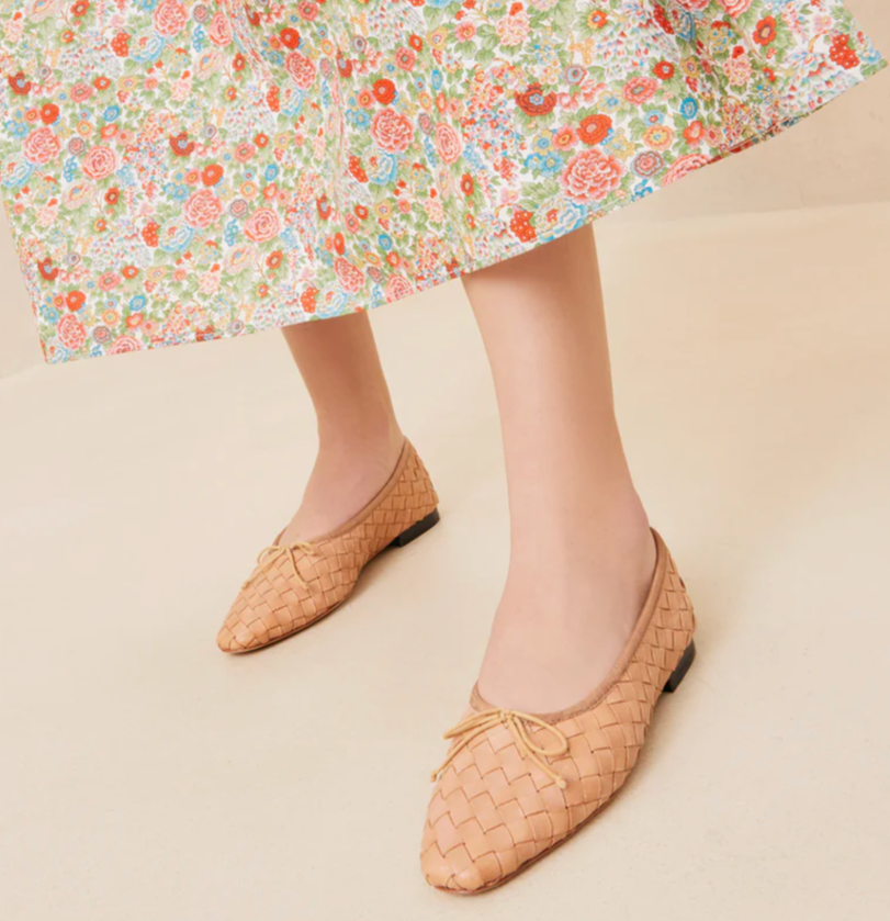 A person standing gracefully on a light surface showcases the Loeffler Randall Landry Woven Flats, paired with the elegant lower part of a floral skirt.