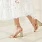 A person in a white lace dress walks indoors on a light-colored floor wearing Loeffler Randall's Malia Curved Heel Sandals, featuring an adjustable ankle strap.