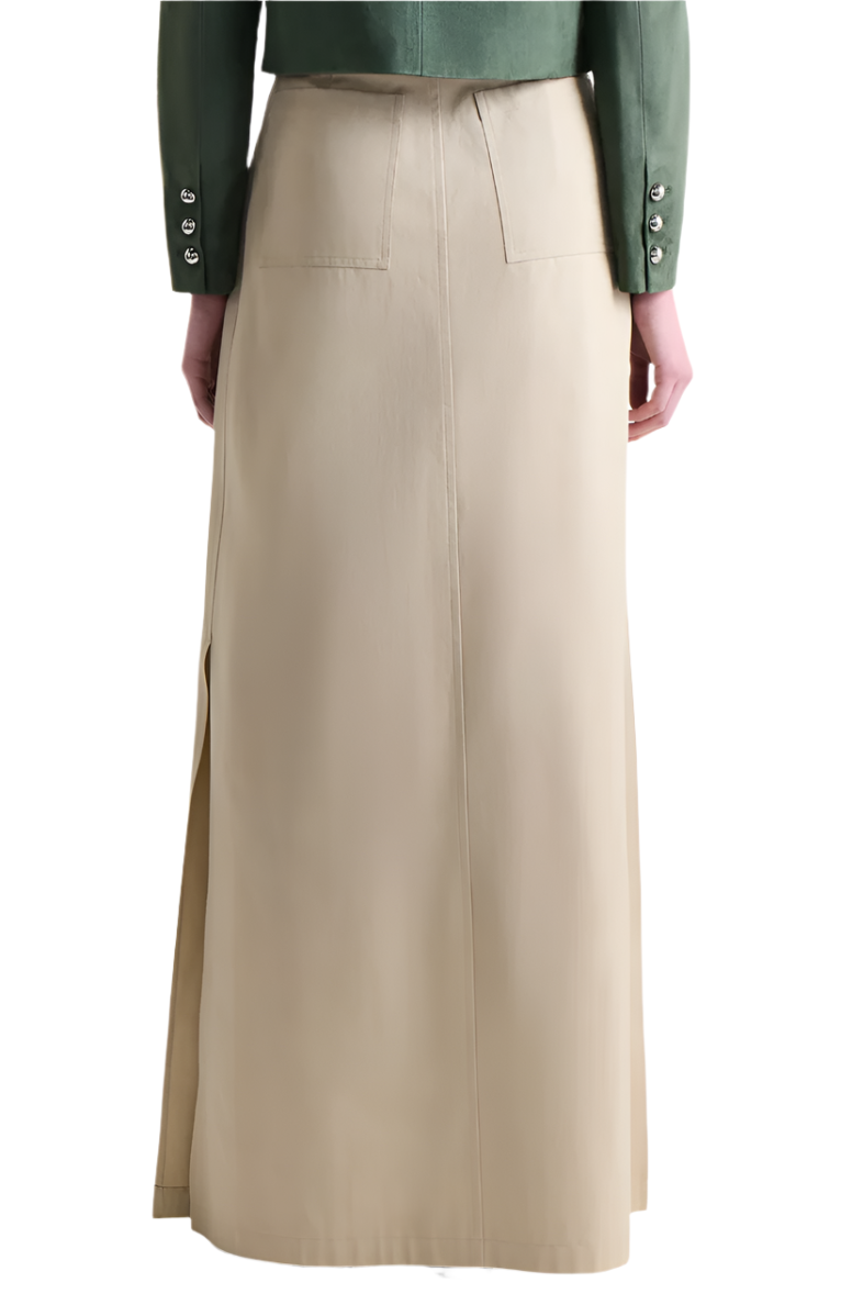 Back view of a person wearing the Altuzarra Mack Skirt, an Italian-made long beige skirt with a voluminous silhouette, two back pockets, and side slits, paired with a green jacket.