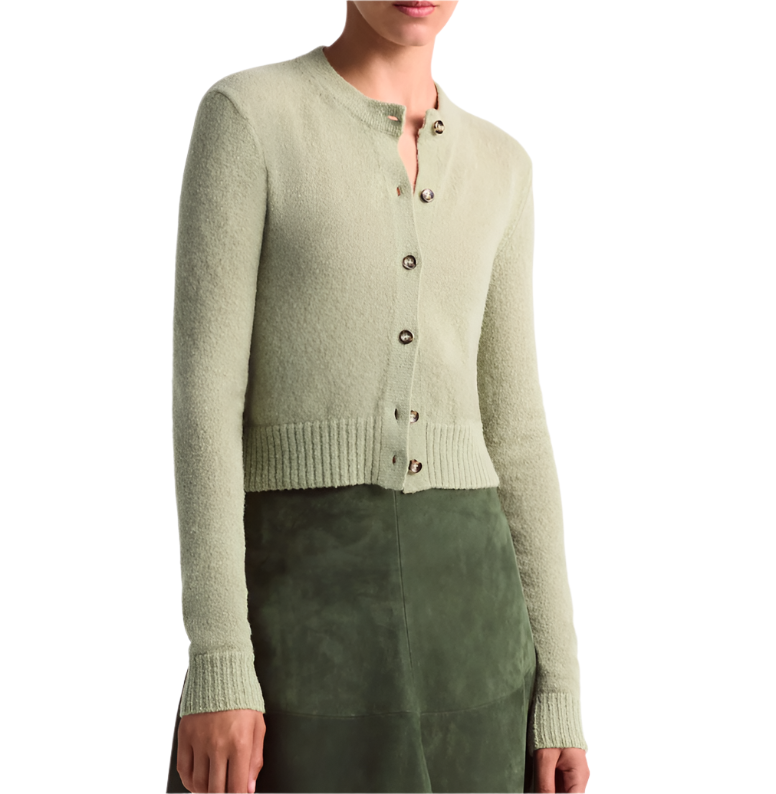 A person wearing the Altuzarra Thea Sweater, a merino wool-blend light green button-up cardigan with ribbed edges, and an olive green skirt, shown from the shoulders to mid-thigh.