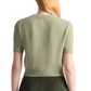 Wearing the Altuzarra Ty Sweater, a person is depicted from behind, showcasing its light green color and close-fitting silhouette. Their long, light-colored hair flows down their back, while the sweater's ribbed hem adds a sophisticated touch to its design.