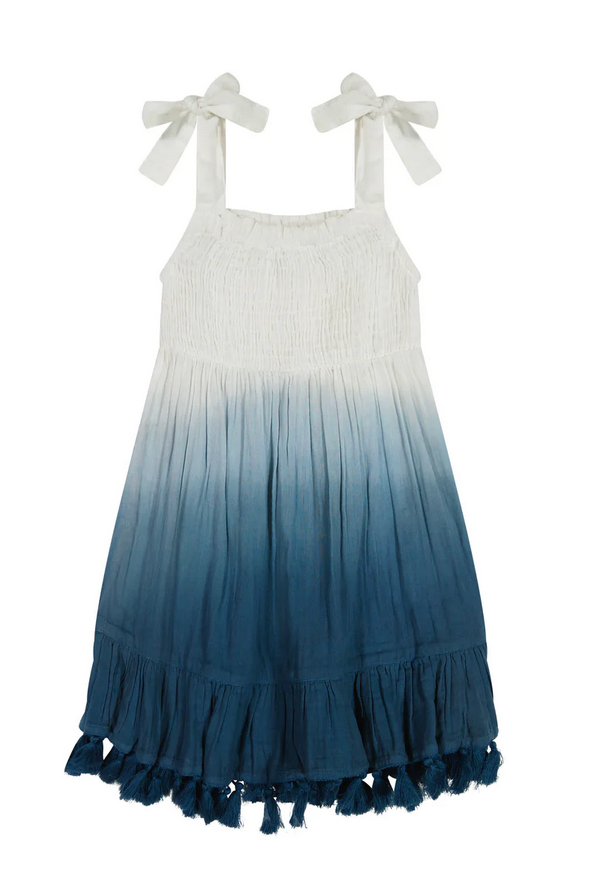 The Mer St Barth Maya Girls Shoulder Tie Sundress by Mer is a sleeveless ombre smocked dress with a white top fading into blue, featuring charming shoulder ties and a flouncy hem adorned with playful tassels.