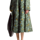 A person is wearing a long-sleeve green marbled floral print midi dress and holding a black bag from Altuzarra's Varda Skirt collection.