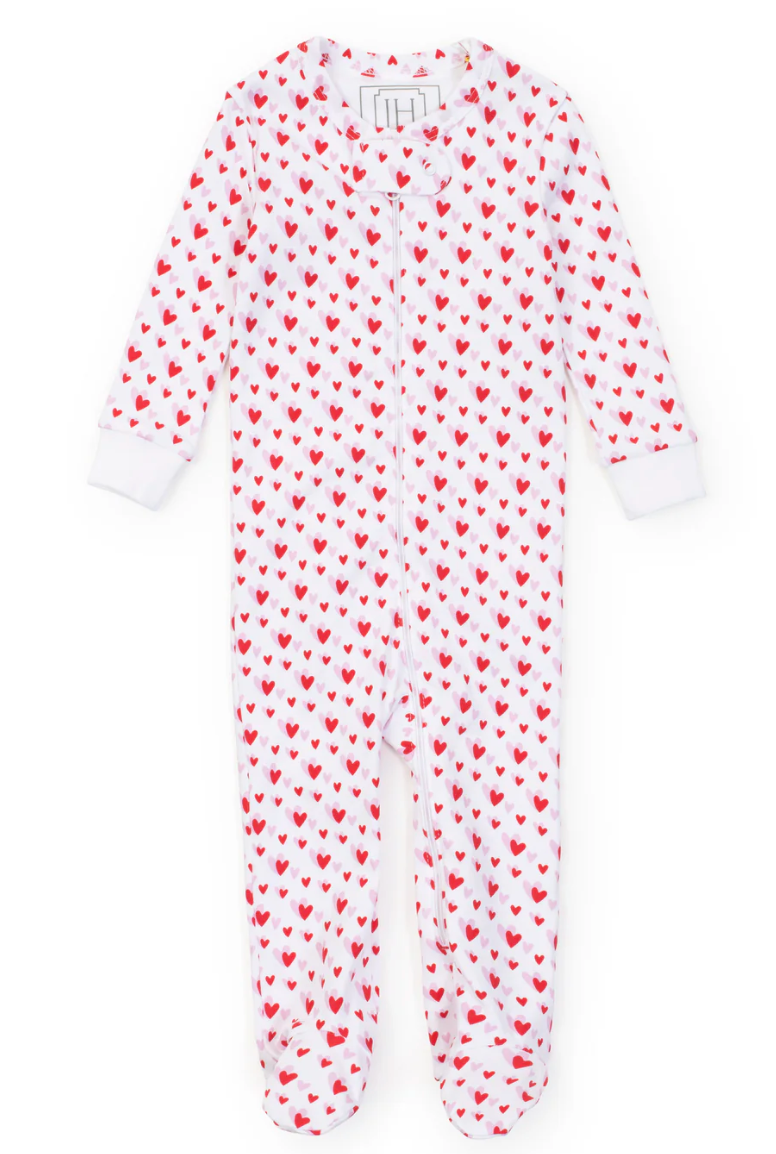 The Lila & Hayes Parker Onesie is a white infant sleeper made from soft Peruvian Pima cotton with a charming red heart pattern, front zipper, and white cuffs, offering cozy comfort for babies.