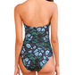 A woman with long wavy hair is seen from the back wearing the Ulla Johnson Monterey Maillot One Piece, a strapless swimsuit with a green and blue tropical leaf pattern and full-coverage bottom.