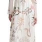A person elegantly wears the Altuzarra Sybbeline Dress, a long sheer silk piece adorned with colorful abstract designs and text, paired with beige shoes. The dress's maxi hem gracefully touches the floor against a plain background.