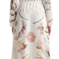 A woman is seen from behind wearing the Altuzarra Sybbeline Dress. This silk maxi dress, decorated with vibrant nature-themed illustrations of animals and flowers, drapes elegantly behind her.