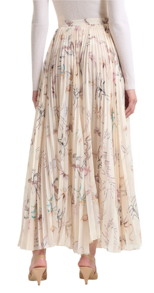 A person is stylishly showcasing the chic Altuzarra Sif Skirt, a pleated mid-length floral design, paired gracefully with a white long-sleeve top and complemented by beige heels.