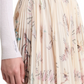 Someone wearing a white ribbed top paired with Altuzarra's Sif Skirt, which showcases a delicate floral and text design in a pleated mid-length style.