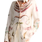 The Altuzarra Chika Top, featuring a white design with botanical and nautical illustrations, pairs seamlessly with crisp white pants and a silver necklace for a relaxed style. Its button front closure adds subtle elegance to the ensemble.