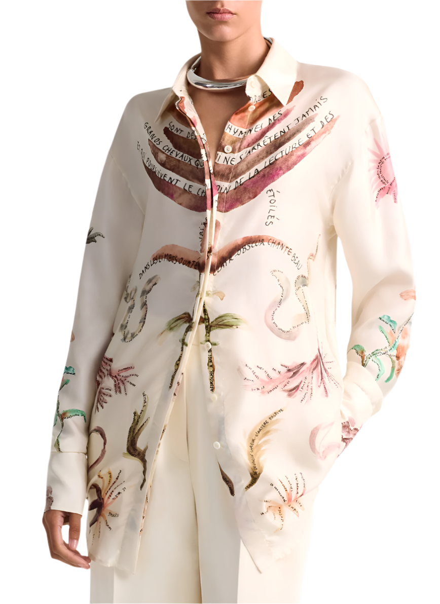 The Altuzarra Chika Top, featuring a white design with botanical and nautical illustrations, pairs seamlessly with crisp white pants and a silver necklace for a relaxed style. Its button front closure adds subtle elegance to the ensemble.