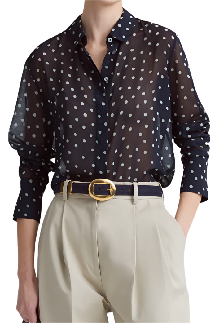 A person wears a sheer navy polka dot blouse tucked into high-waisted beige trousers, cinched with the Altuzarra Vintage Brass Buckle Belt.