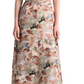 A person wearing the Altuzarra Honey Dress—a patterned, short-sleeve, ankle-length silk dress with a draped waist—paired with black heeled shoes featuring an oversized buckle.