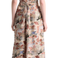 A woman faces away, wearing the Altuzarra Honey Dress—a mid-length, short-sleeve silk dress with a multicolored nature-inspired print—and black heeled sandals with an oversized buckle.