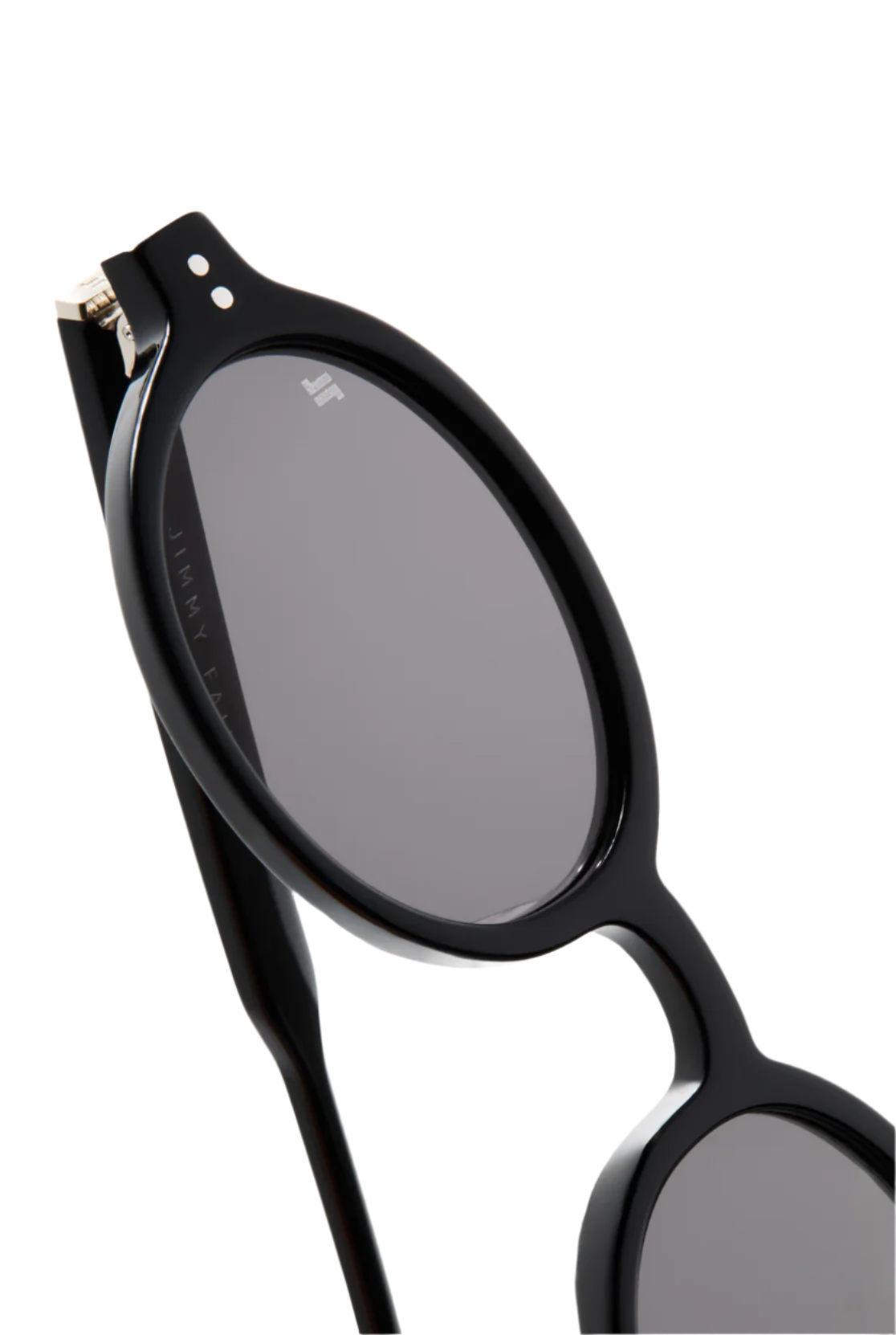 Close-up of Elvie Sunglasses by Jimmy Fairly: black oval frame crafted from cellulose acetate, with dark lenses, sturdy metal hinges, and a small white logo on the top left lens.