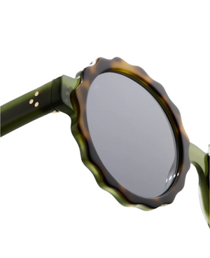 Close-up of Lily Sunglasses by Jimmy Fairly: round shape, dark lenses, green arms, scalloped tortoiseshell-patterned cellulose acetate frame, and sturdy metal hinge.