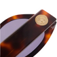 Close-up of the arm of the Jimmy Fairly Meli Icons Sunglasses, showcasing a cellulose acetate tortoiseshell-pattern with a gold medallion and purple lenses.