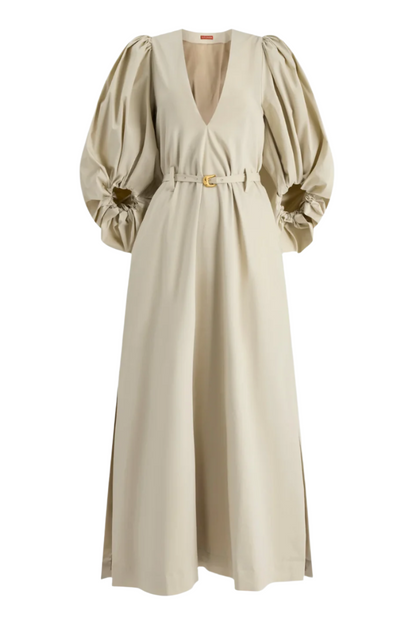 The Altuzarra Corrie Dress is a beige maxi with voluminous sleeves, a deep V-neck, belted waist, and side slits for a chic silhouette.
