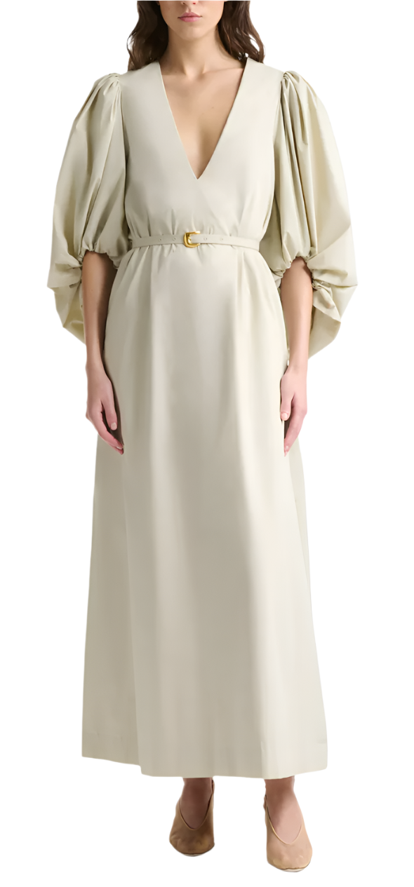 A woman wears the Altuzarra Corrie Dress, featuring voluminous sleeves, a deep V-neckline, a belted waist, and floor-length design, paired with nude flats.