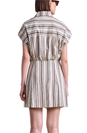 A woman in the Apiece Apart San Vito Sarong Dress, a short-sleeved, collared striped mini dress with a flattering fit, stands facing away from the camera wearing sunglasses.