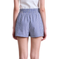 Model wearing Apiece Apart Surf Shorts—blue-and-white vertical stripes, pull-on style—paired with a white shirt and shown from the back against a plain background; perfect for warm days.