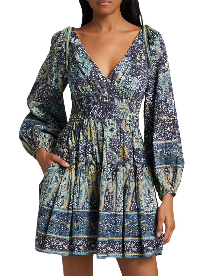 A woman wears the Ulla Johnson Anika Dress, a patchwork print mini dress with blouson sleeves, V-neckline, smocked waist, and pockets.