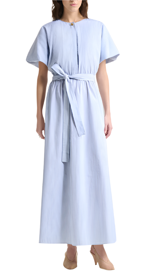 A woman wears the Paulina Banker Stripe Dress by Altuzarra—a light blue cotton poplin shirt dress with vertical stripes, short kimono sleeves, a tied waist belt—and beige heels.