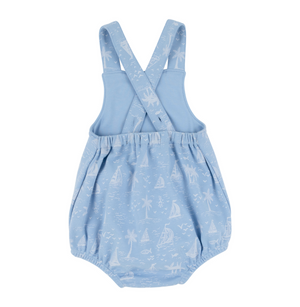 The Beaufort Bonnet Company's Baby Stillman Sunsuit is a light blue romper with cross-back straps, an elastic waistband, and a white Bay Side Boats nautical print featuring sailboats, palm trees, and fish.