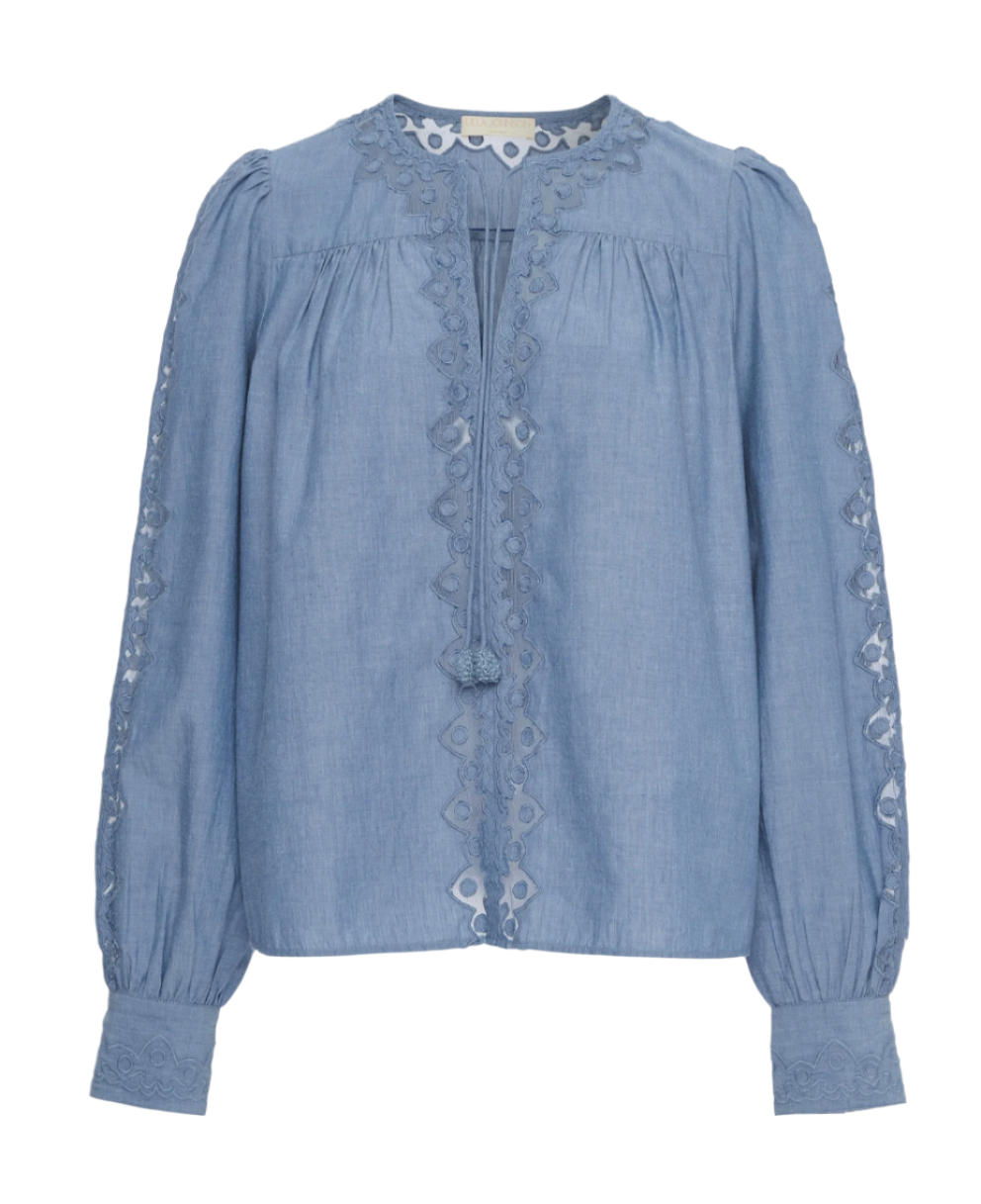 The Kady Blouse by Ulla Johnson is crafted from light blue water-washed cotton with geometric embroidery on the front, sleeves, and cuffs. It features a round neckline and front tassel ties.