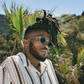 A man wearing Jimmy Fairly's The Noto sunglasses, which have a lightweight acetate frame, stands outdoors in a patterned shirt amid palm trees and greenery under a clear blue sky.
