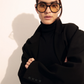 Model wearing The Lars oversized yellow-tinted sunglasses by Jimmy Fairly, featuring a bold cellulose acetate frame, paired with a black turtleneck and blazer, standing against a light background with arms crossed.