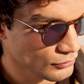 Close-up of a person with curly hair wearing The Emilio sunglasses by Jimmy Fairly, featuring brown acetate frames and looking slightly downward.