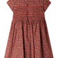 The Bonpoint Girls' Duchesse Smocked Dress made with Liberty Fabric features short sleeves, a knee-length cut, red and pink floral print, embroidered smocking on the bodice, and a gathered skirt.