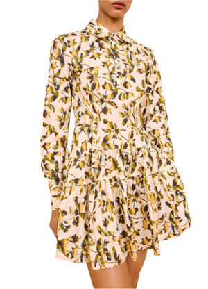 A woman wears the Ulla Johnson Nanette Mini Dress—a long-sleeve, collared poplin dress with yellow and green graphic blooms on a light background.