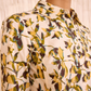 Close-up of a person wearing the Ulla Johnson Nanette Mini Dress, featuring a collared neckline and a yellow, green, and brown leaf print reminiscent of graphic blooms, set against a light background.