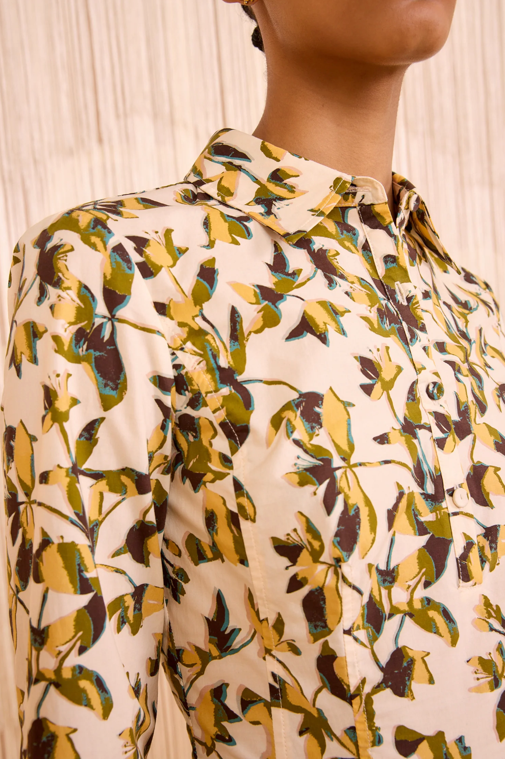 Close-up of a person wearing the Ulla Johnson Nanette Mini Dress, featuring a collared neckline and a yellow, green, and brown leaf print reminiscent of graphic blooms, set against a light background.