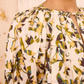 Close-up of a person wearing the Loli Top by Ulla Johnson, a cream-colored cotton poplin blouse featuring yellow, green, and brown abstract floral prints, gathered neckline details, and subtle puff sleeves.