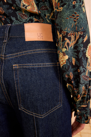Wearing Ulla Johnson’s Genevieve High Rise Jean in vintage-inspired indigo with a tan patch, paired with a floral patterned shirt.