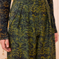 A person wearing Ulla Johnson’s Charlie Silk Pant—high-waisted, wide-leg trousers in dark green ikat animal print—paired with a matching long-sleeve top.
