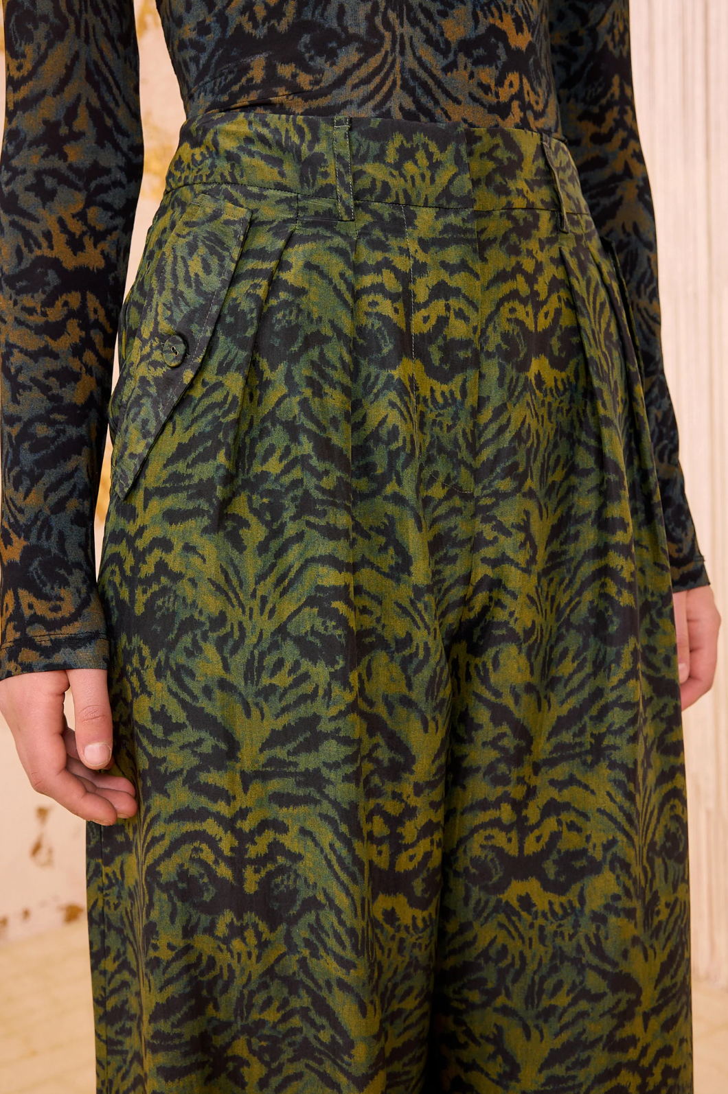 A person wearing Ulla Johnson’s Charlie Silk Pant—high-waisted, wide-leg trousers in dark green ikat animal print—paired with a matching long-sleeve top.