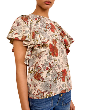 A person wears the Ulla Johnson Lena Flutter Sleeve Blouse with floral print and ruffled shoulders, paired with blue jeans, shown from the chest up.