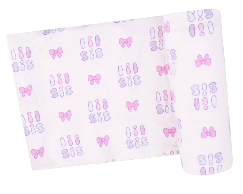 The Angel Dear Swaddle Blanket is a white viscose from bamboo swaddle with a repeating “sis” pattern in purple and pink, plus pink and purple bows and ovals.