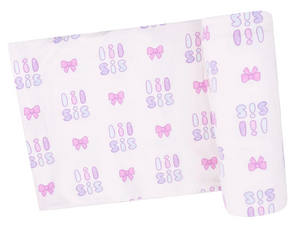 The Angel Dear Swaddle Blanket is a white viscose from bamboo swaddle with a repeating “sis” pattern in purple and pink, plus pink and purple bows and ovals.