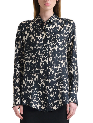 A woman wearing the Chika Top by Altuzarra—a relaxed, long-sleeve silk blouse with a black and white abstract spotted pattern and concealed buttons—stands against a plain background.