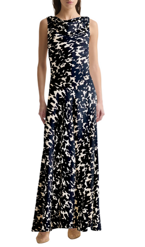 A woman stands against a white background wearing the Altuzarra Drina Dress—a sleeveless, floor-length silk gown with a black and white abstract pattern—paired with beige shoes.