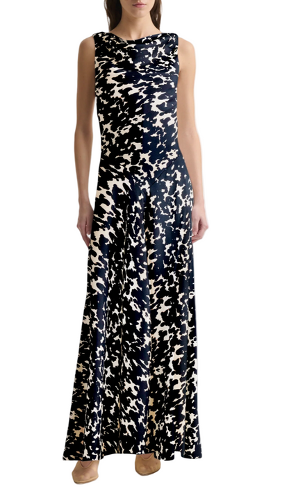 A woman stands against a white background wearing the Altuzarra Drina Dress—a sleeveless, floor-length silk gown with a black and white abstract pattern—paired with beige shoes.