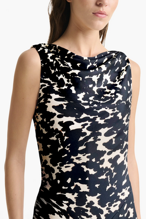 A woman wears the Altuzarra Drina Dress, a sleeveless silk dress with a black and beige tortoise print and draped neckline.