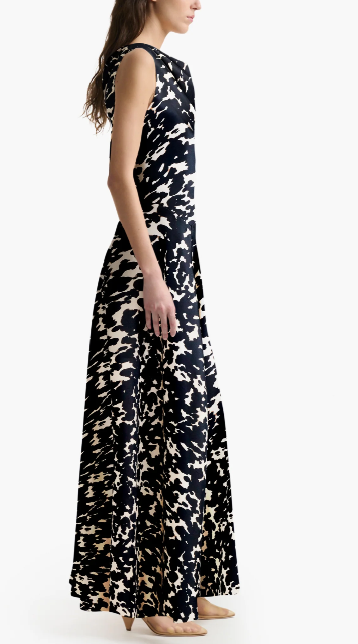 A woman in profile models the Altuzarra Drina Dress, a sleeveless, floor-length black-and-white abstract silk gown, paired with beige heels against a plain white background.
