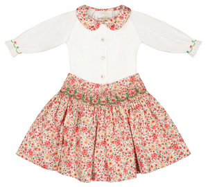The Antoinette Girls' Marie Red Floral Smocked Skirt and Blouse Set features a white, long-sleeved, embroidered-collar blouse and red floral smocked skirt—perfect as a holiday outfit for girls.
